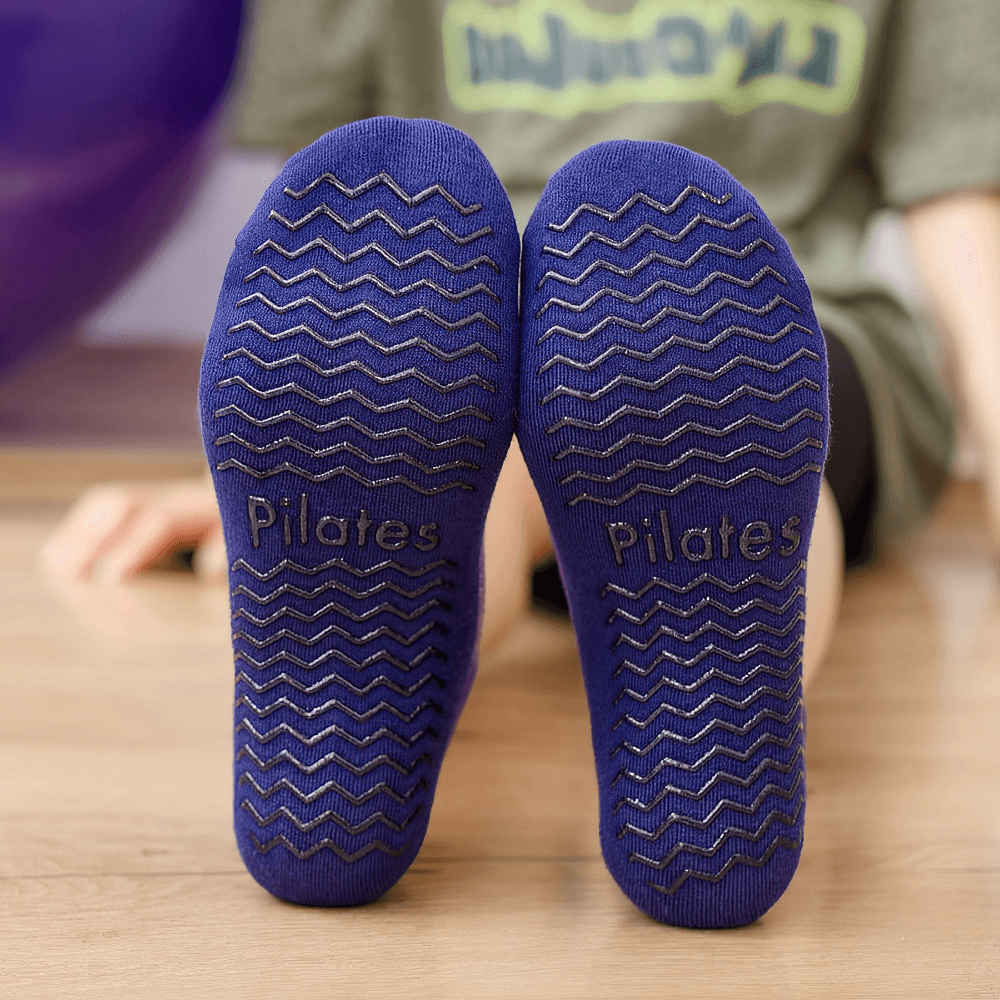 Person wearing blue non-slip yoga socks with Pilates grips on a wooden floor.